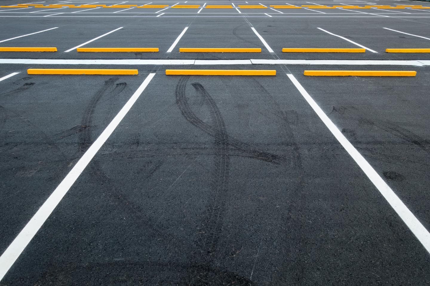 A freshly paved commercial asphalt parking lot with crisp white line striping and bright yellow wheel stops in empty stalls.